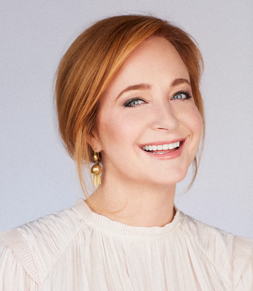 Professional headshot of Claire Spaht, with cream colored blouse, gold earrings and red hair.